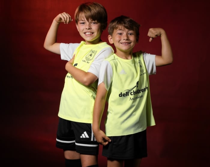 Two young boys in yellow soccer jerseys pose flexing arms against a red background