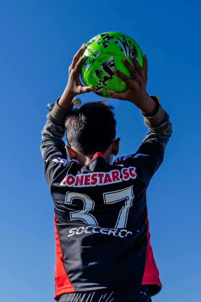 Soccer player in black jersey preparing a throw-in with a bright green ball
