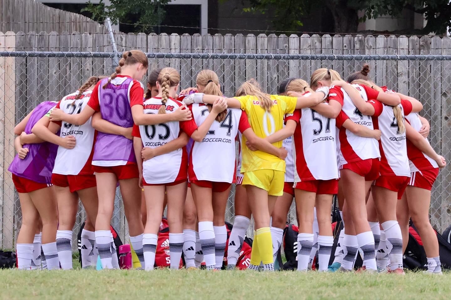 Girls youth soccer team huddling together on the field before a game in red and white uniforms