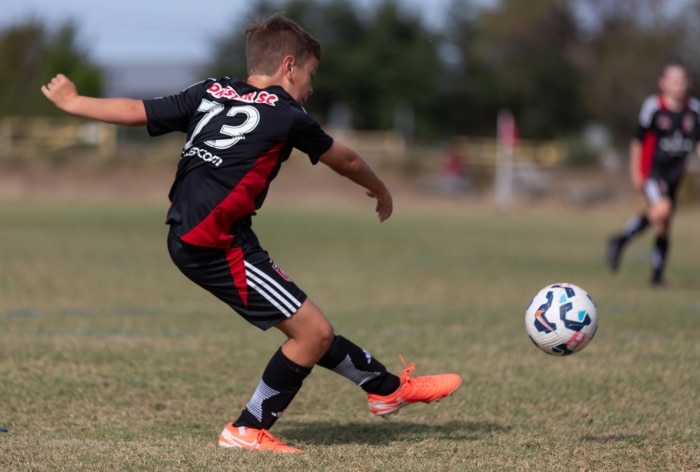 Youth soccer player kicking a ball on a field during a match