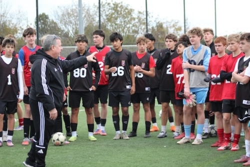 Soccer coach instructing teenage players during practice on a green field