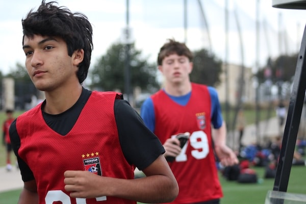 Teen soccer players jogging on field wearing red practice jerseys