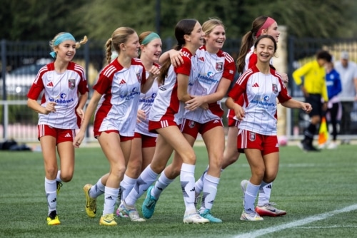 Youth girls soccer team celebrating on the field in red and white uniforms