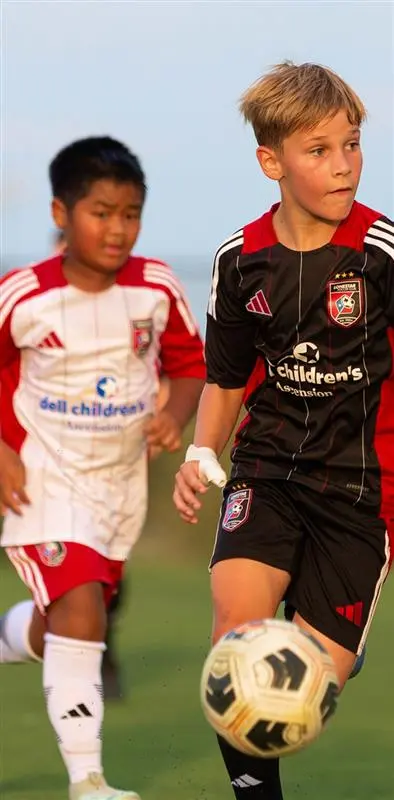 Two young boys playing soccer on a field in colorful team uniforms