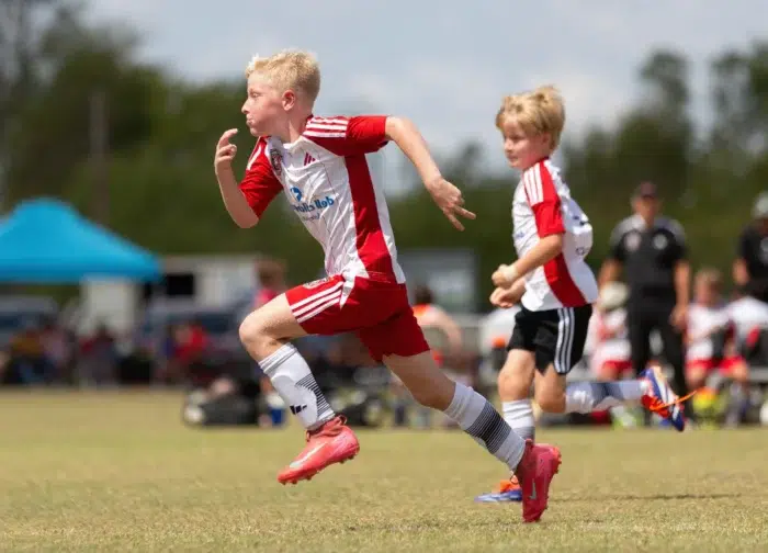 Young boys sprinting in a soccer match on sunny day
