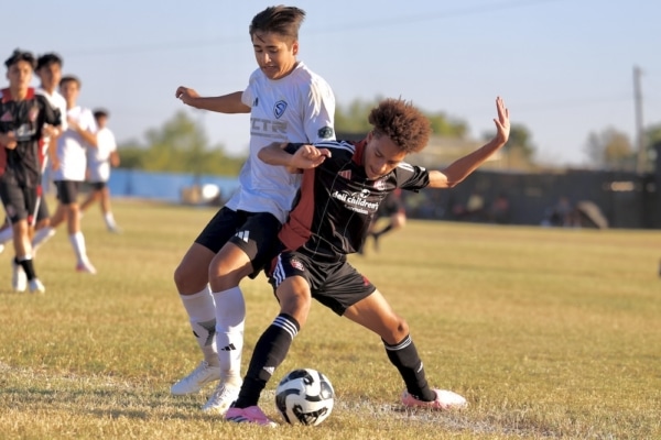 Two soccer players compete for the ball during a match on a grassy field.