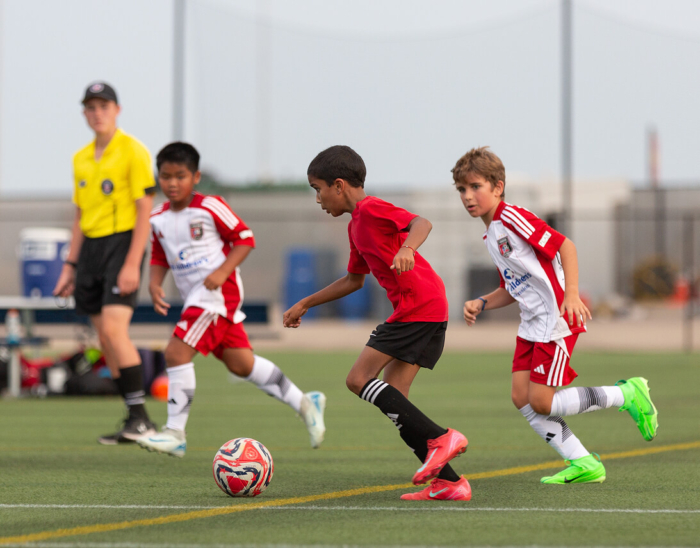 Youth soccer game with kids playing on the field and a referee in the background.