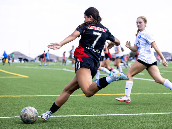 Soccer player in a red and black jersey kicking a ball on a field during a match with opponents nearby