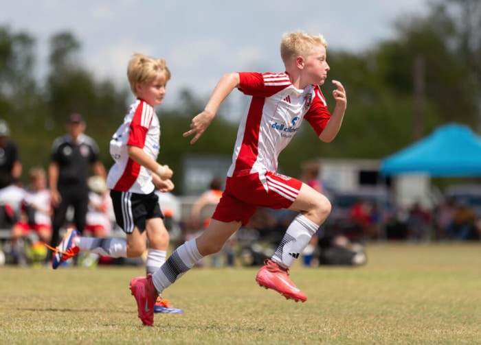 Young boys in red and white uniforms playing soccer on a sunny day