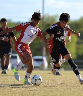 Two young soccer players compete for the ball on a sunny field during a match.