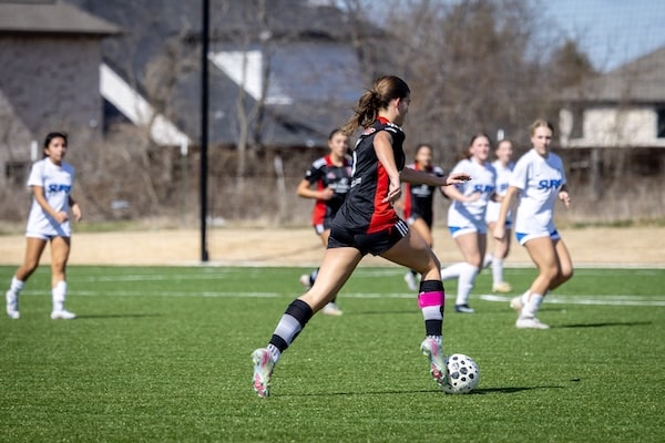 Female soccer player in black jersey dribbles ball during a youth match on green field