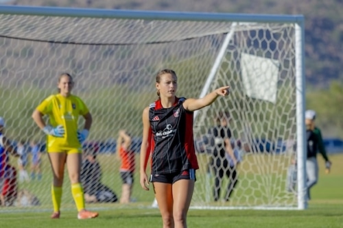 Soccer player in black jersey pointing on field near goal and teammates