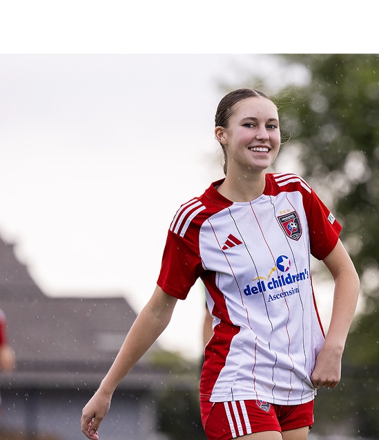 Smiling soccer player in red and white uniform on the field.