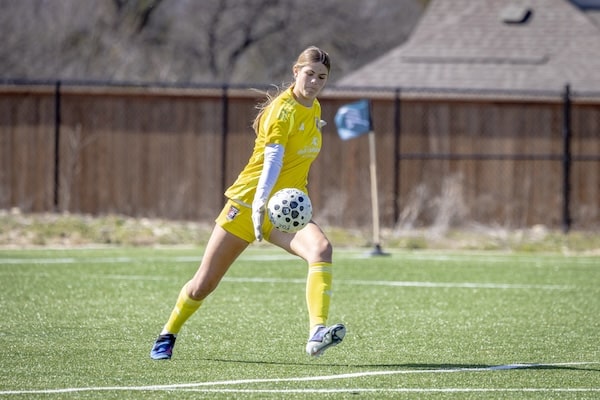 Soccer player in yellow jersey kicking a ball on a sunny field