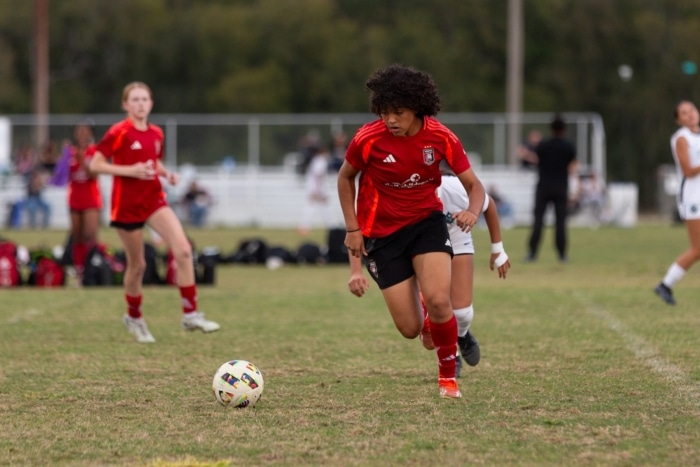 Soccer player in red jersey dribbling the ball on a grass field during a game