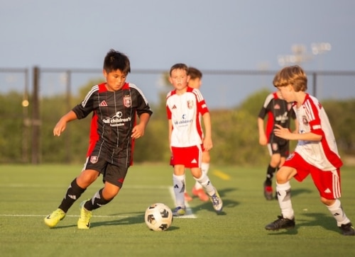 Children playing soccer on a field during a sunny day in team uniforms.