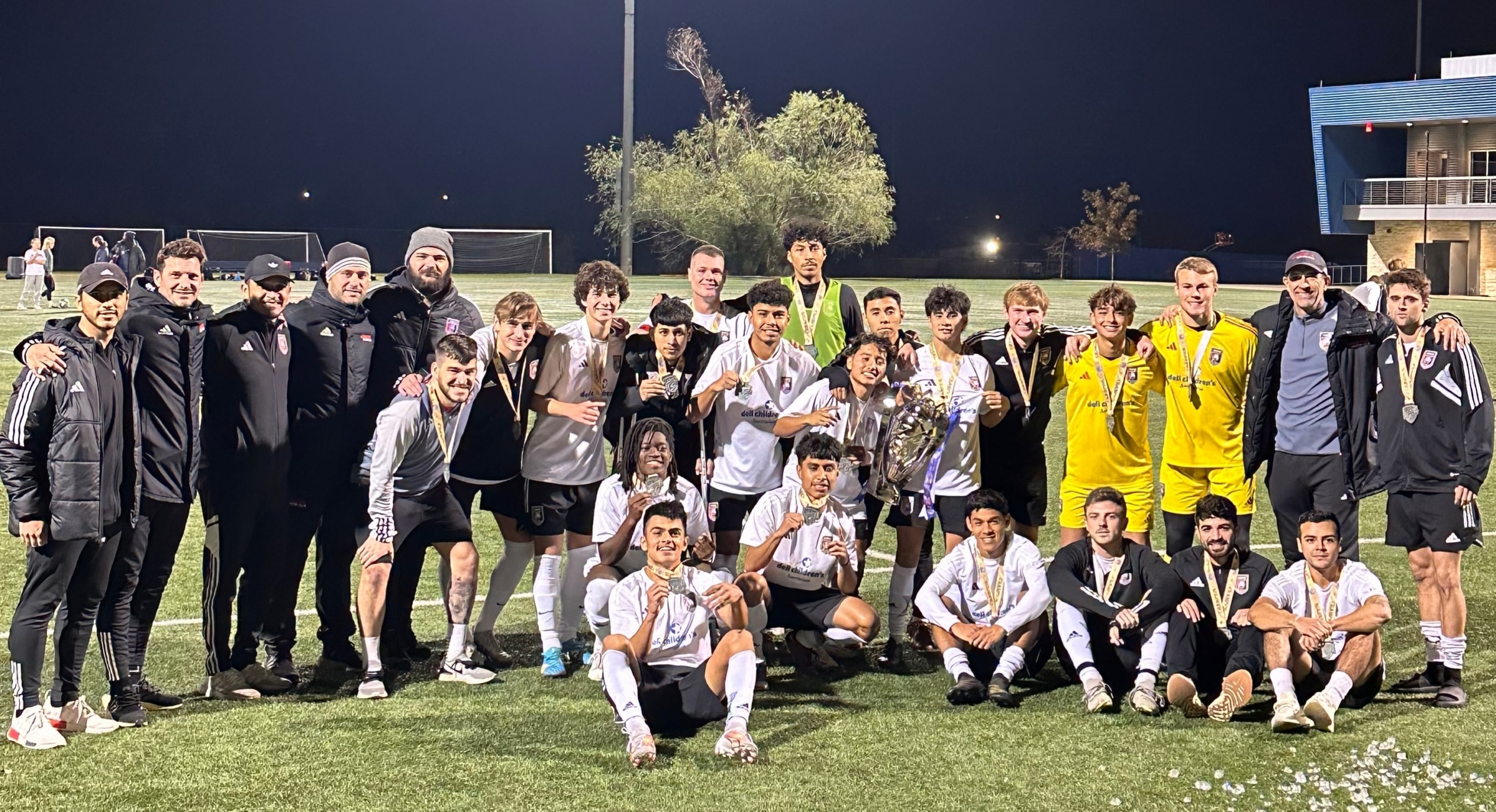 Soccer team celebrates with medals and trophy on the field at night